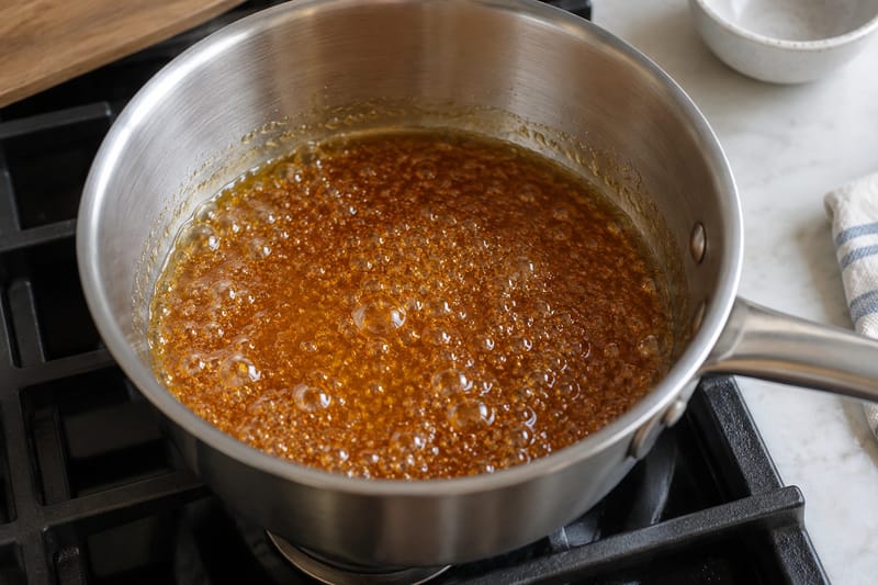 Karamel lavet med vand får ravfarve i en gryde med lys inderside. Karamel lavet med vand får ravfarve i en gryde med lys inderside.