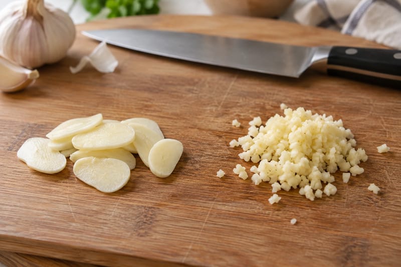 Dunne plakjes knoflook naast fijngehakte knoflook op een snijplank. Dunne plakjes knoflook naast fijngehakte knoflook op een snijplank.