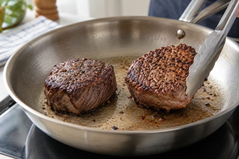Steaks searing in a roomy pan with browned surfaces and space between them.