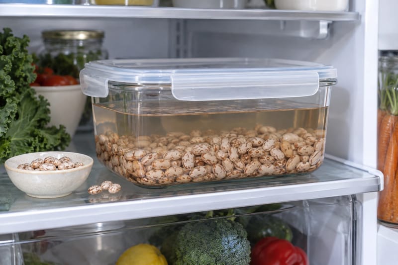Getrocknete Bohnen weichen vollständig mit Wasser bedeckt in einem abgedeckten Behälter im Kühlschrank ein.