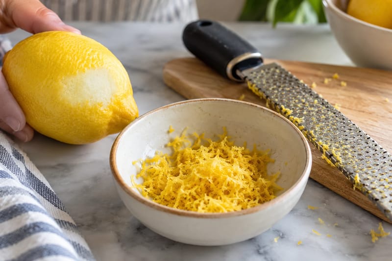 A partly zested lemon beside finely grated yellow zest. A partly zested lemon beside finely grated yellow zest.